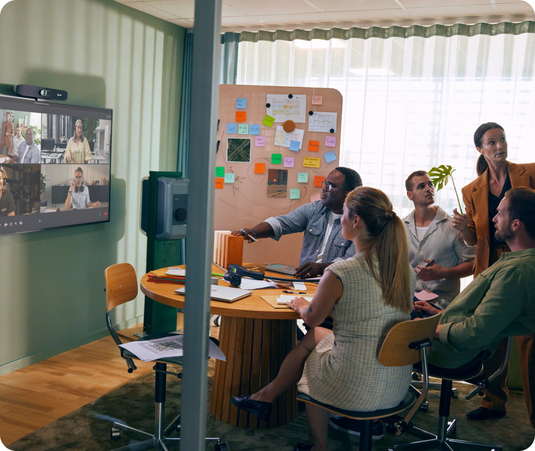 Team collaborating in small meeting room with colleagues on video call