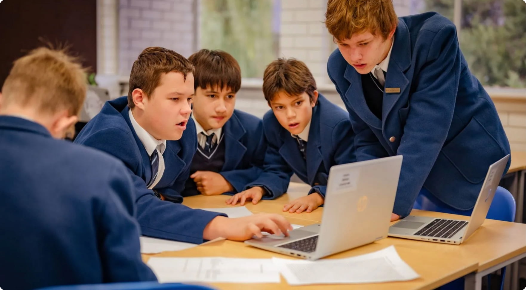 Five Mazenod schoolboys gathered at table using HP laptops for school work