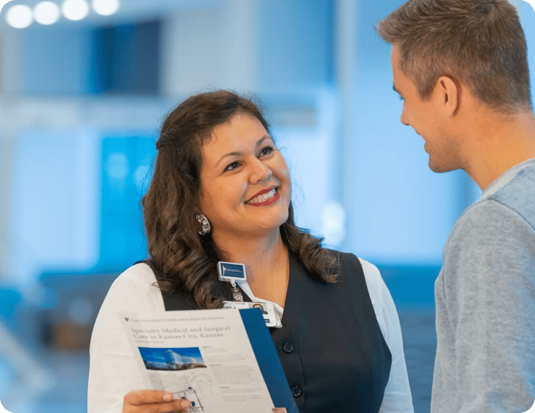 Woman in a dark vest and ID badge speaks with a man while holding a clipboard in a modern business environment, representing positive HP customer service experience.