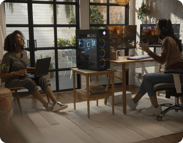 Two people laughing and gaming on dual monitors and a laptop.